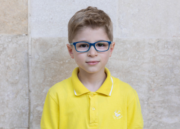 Blond chłopiec w żółtej koszulce polo i w okularach z niebieskimi oprawkami.